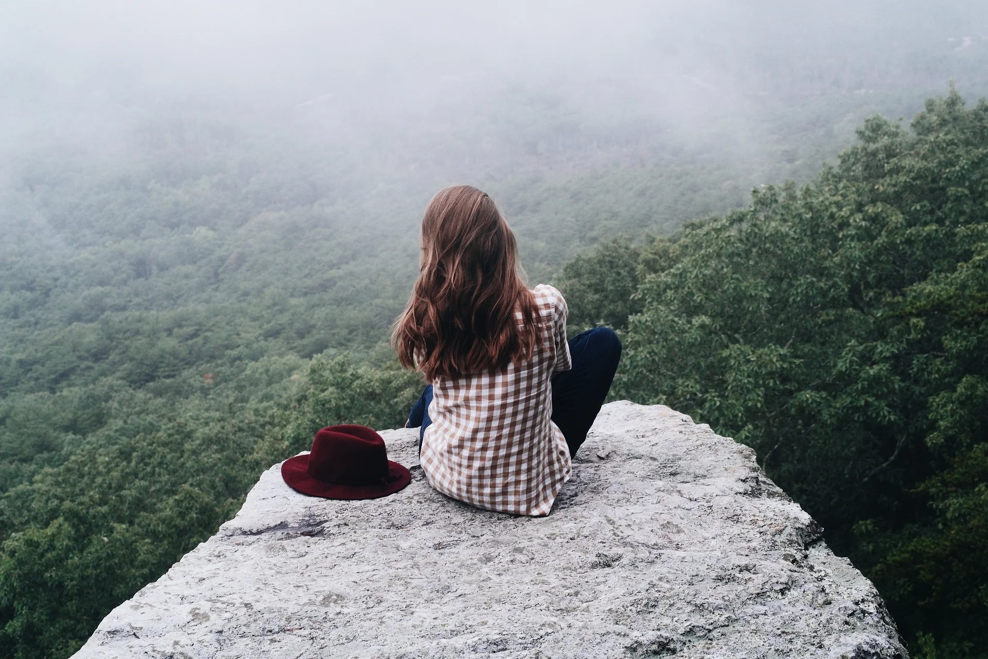 Woman sitting with hat on high ledge looking out at fog