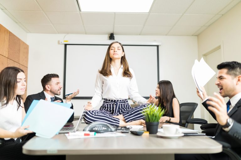 Woman sitting on workplace desk with coworkers shouting