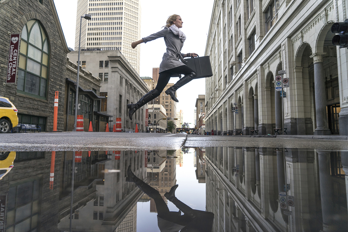 Woman jumping across street with puddle