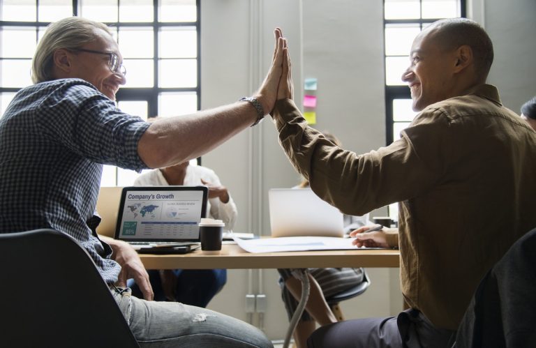 Two men in workplace high five with hands